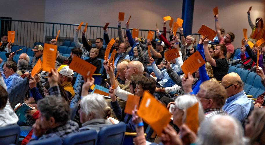Bow residents raise their voting cards to pass warrant article five at the town meeting at the auditorium of the high school on Wednesday night, March 13, 2024.