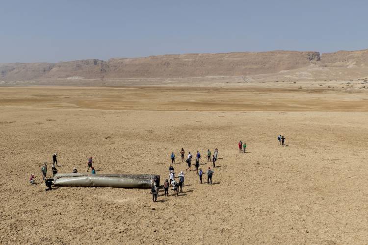 People gather around a component from an intercepted ballistic missile that fell near the Dead Sea in Israel, Saturday, April 20, 2024. Open fighting between Israel and Iran began April 1 with the suspected Israeli killing of Iranian generals at an Iranian diplomatic compound in Syria.