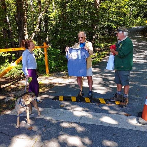 Cheered on by his daughter, Lynsey, and her dog, Berlioz, John Burke of Peterborough receives a t-shirt from Pack Monadnock Staff, marking his 81st climb in 81 days, in celebration of his 81st birthday.