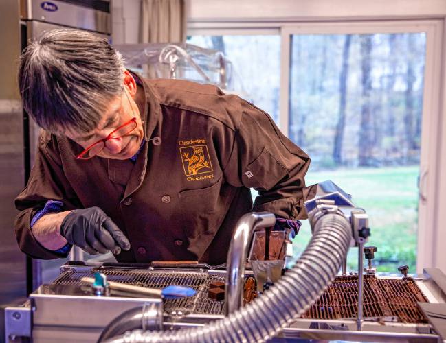 Chocolatier Jonathan Doherty uses the enrober to coat his base chocolate with another coating of chocolate at his home in Hopkinton on Tuesday.  Doherty worked with the National Parks Service in conservation before retiring and pursuing chocolate-making full-time, which shines through in his creations.