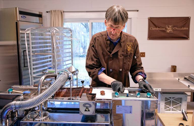 Chocolatier Jonathan Doherty uses the enrober to coat his base chocolate with another coating of chocolate at his home in Hopkinton on Tuesday, April 30, 2024.  Doherty worked with the National Parks Service in conservation before retiring and pursuing chocolate-making full-time, which shines through in his creations.