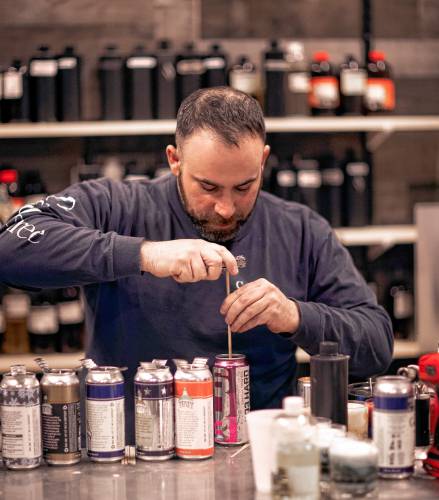 Ross Mingarelli flattens the bottom of cans for his speciality beer can candles at his downtown Candle Tree Soy Candle shop in Concord.