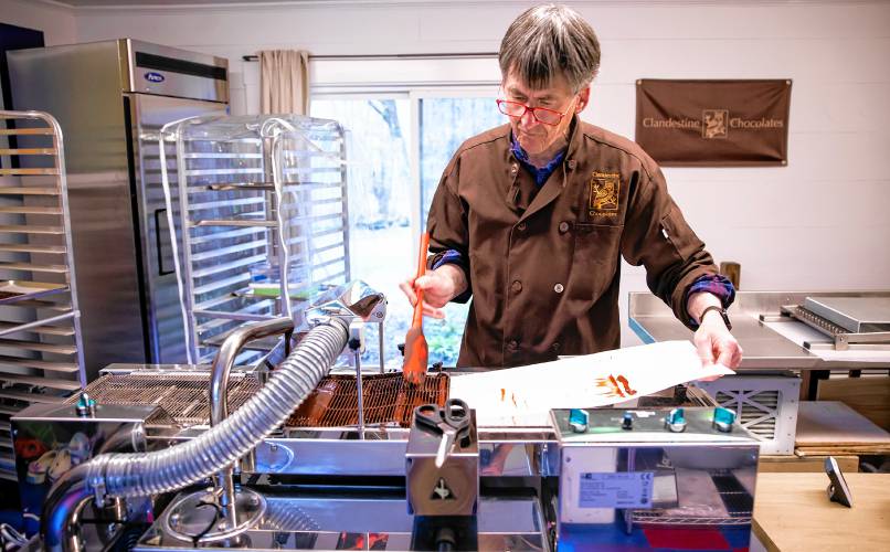 Chocolatier Jonathan Doherty uses the enrober to coat his base chocolate with another coating of chocolate at his home in Hopkinton on Tuesday, April 30, 2024.  Doherty worked with the National Parks Service in conservation before retiring and pursuing chocolate-making full-time, which shines through in his creations.