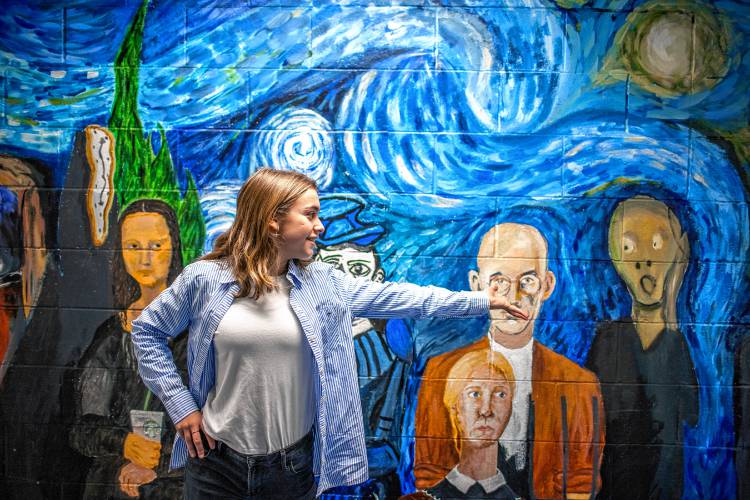 Caia Kimball, a freshman at Concord High School, stands in front of one of the many murals around the school on Friday, December 8, 2023. Kimball wanted to foster the creative arts so she decided to give back resources to the art department Broken Ground School where she went to school.