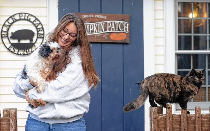 Helen St. Pierre of Old Dogs Go To Helen holds Fletch, the oldest dog she takes care of, as she stands alongside Emily, one of the barn cats at her Epsom farm.